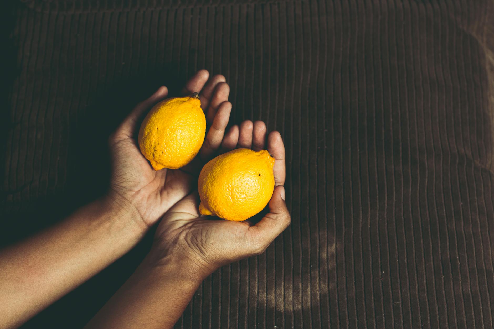 Close-up of two fresh lemons held in cupped hands, symbolizing the gentle suction design of Hello Nancy clitoral vibrators.