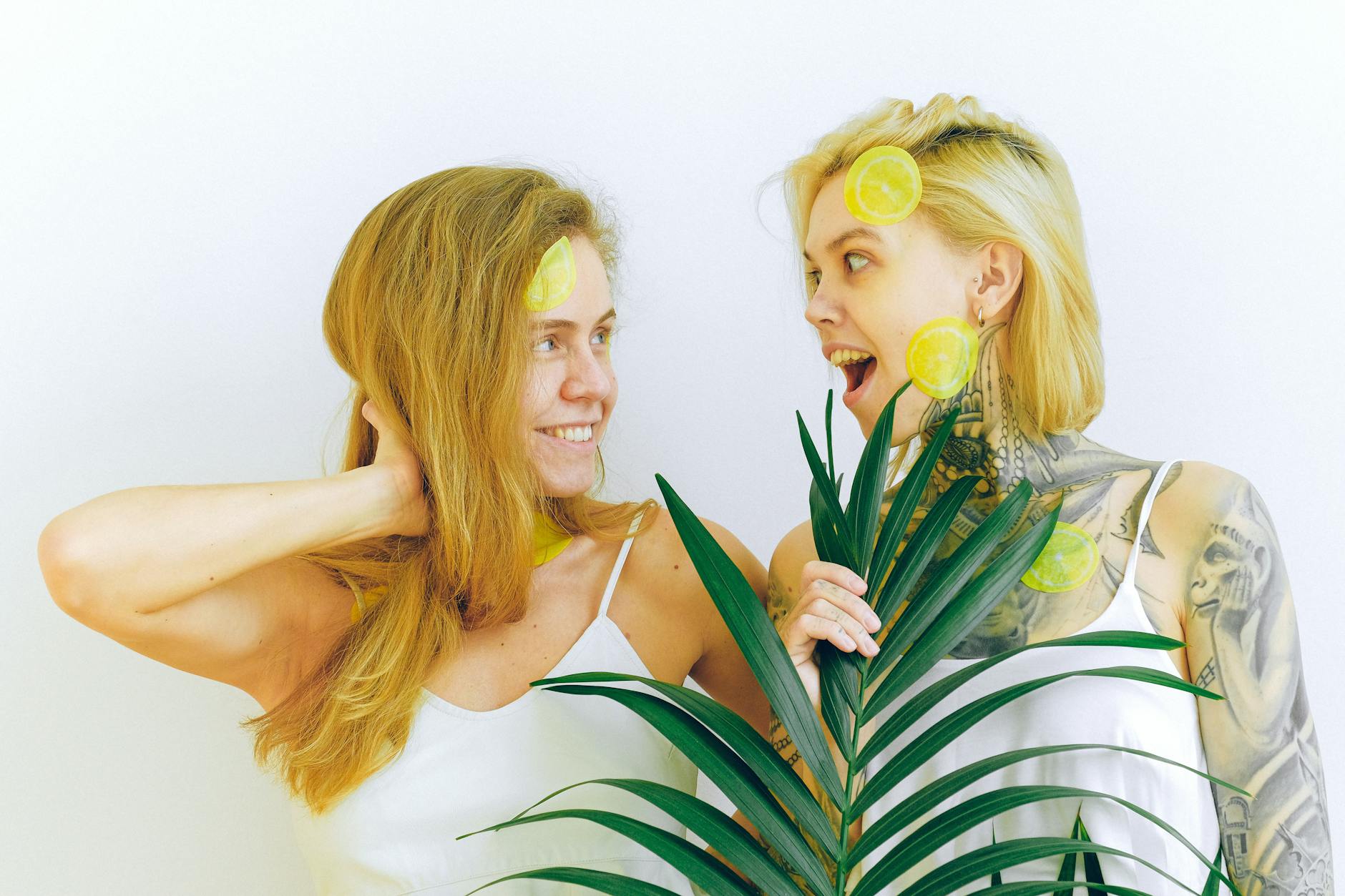 Two women smiling joyfully with lemon slices, expressing confidence and playful energy indoors