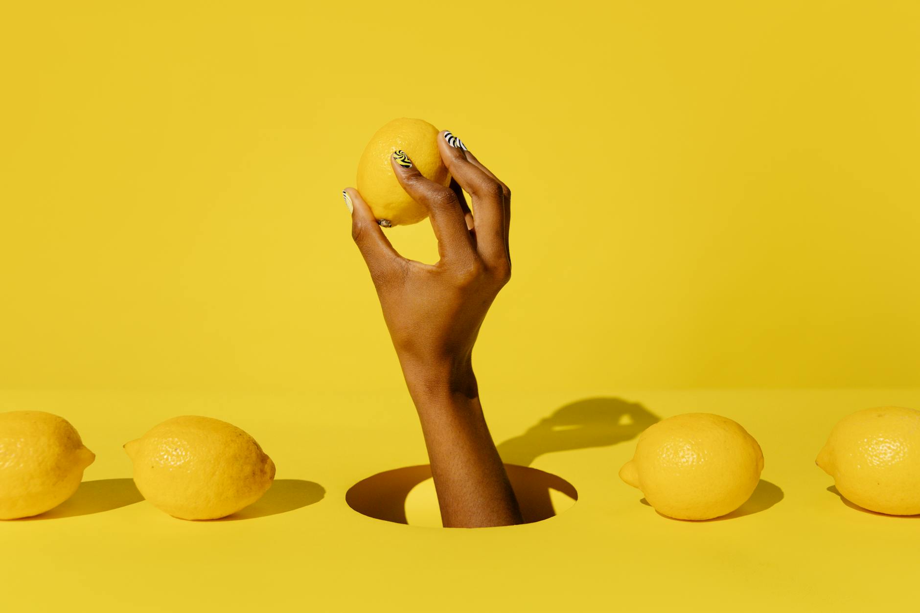 Hand holding a fresh lemon against a vivid yellow background, symbolizing the fresh approach of lemon vibrators