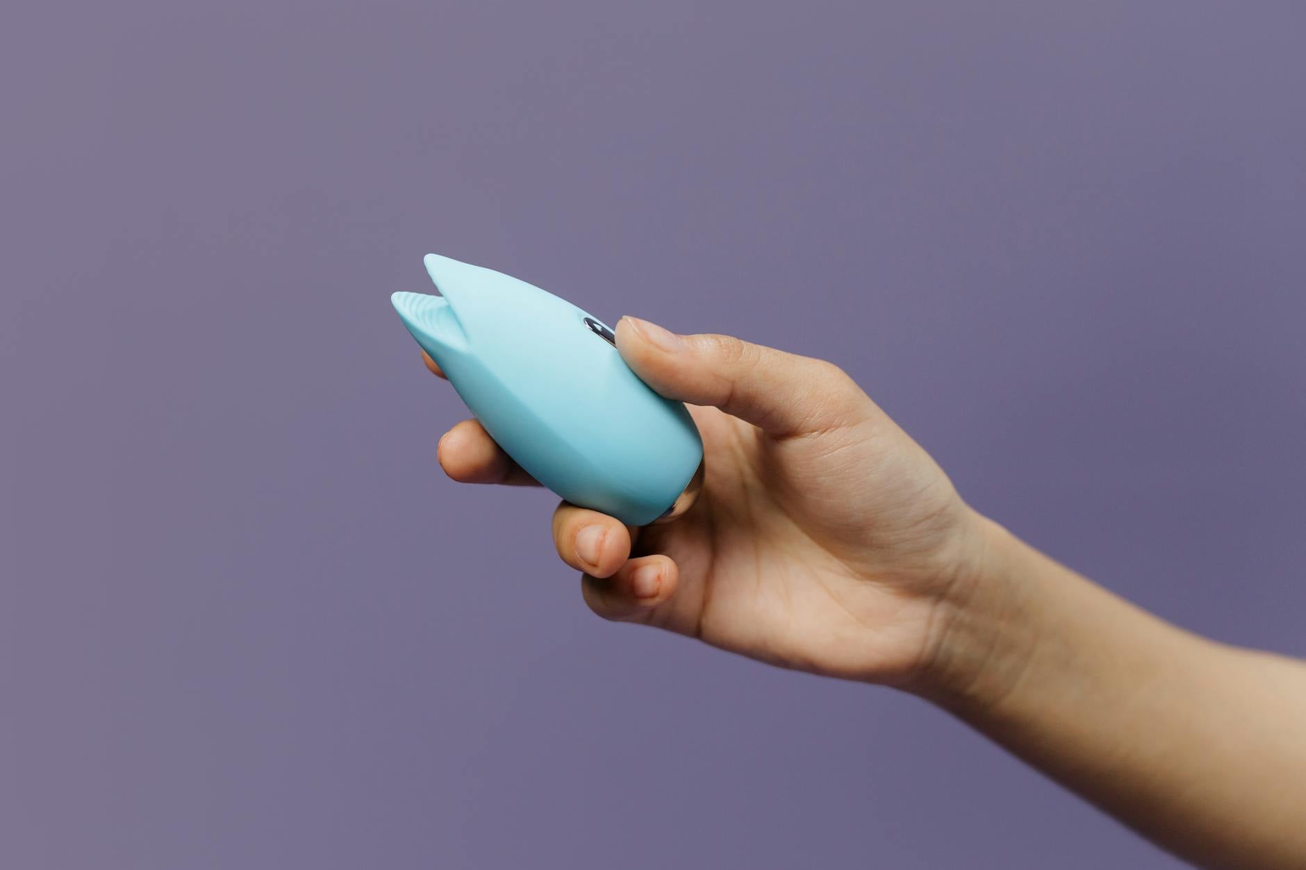 A blue silicone clitoral vibrator held against a purple background, representing modern intimacy tools for long-distance couples.