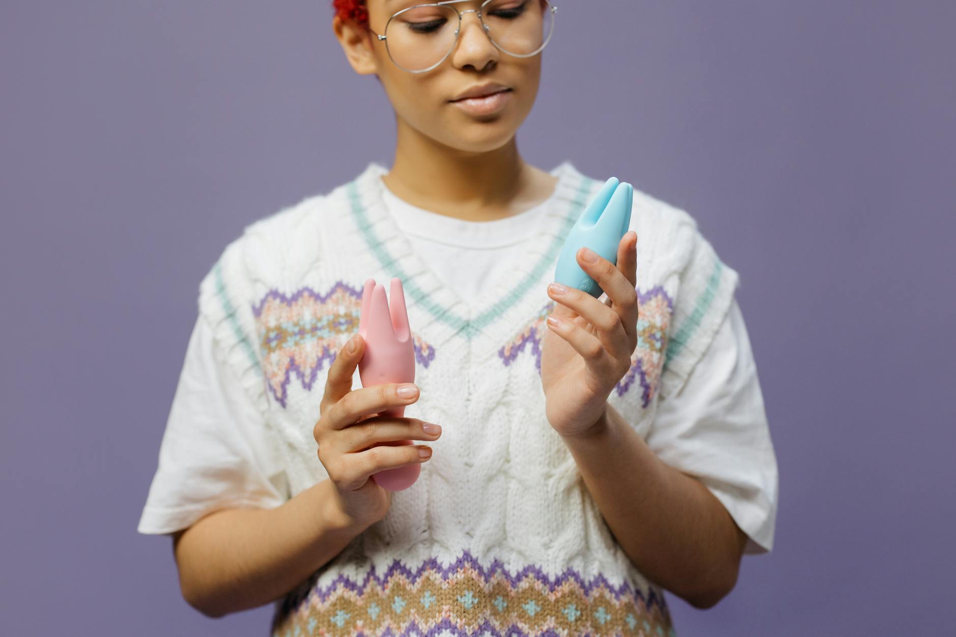 Woman holding blue and pink silicone clitoral vibrators in a thoughtful moment